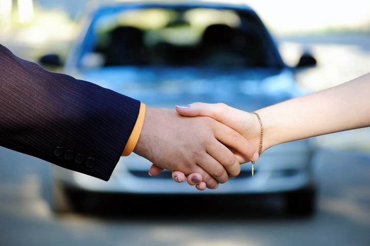 Two people shaking hands in front of a car
