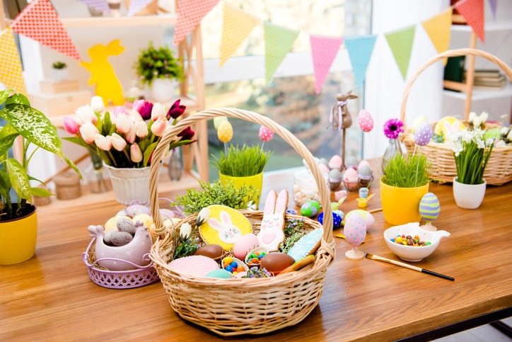 Wooden basket with easter composition, sweets, choco, gingerbread standing on table decorated with easter colored eggs and flowers