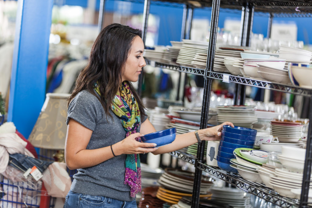 woman looking at the kitchen section of a thrift store, picking up a bowl off a rack