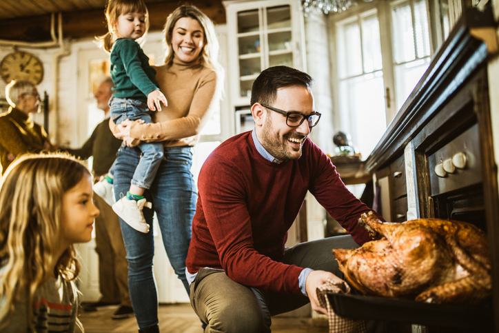 man pulling turkey out of the over while wide and daughter smile behind him