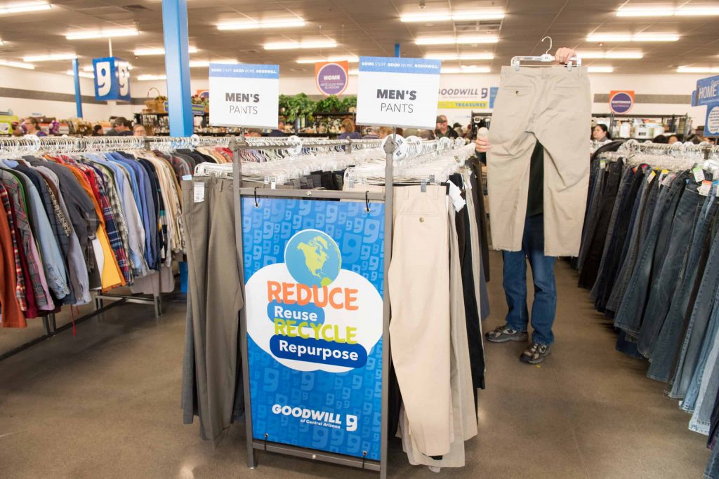 Goodwill AZ | Someone standing inracks of pants holding up a tan pant on a hanger