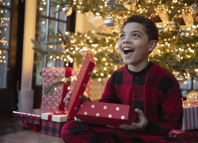 kid excited opening up a present with a christmas tree in the background