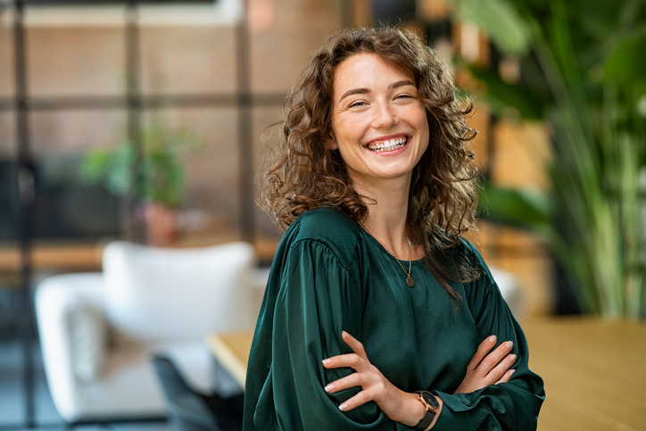 Portrait of young smiling woman looking at camera with crossed arms. 