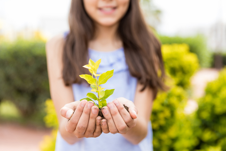 Young girl protecting small plant on Earth Day in garden