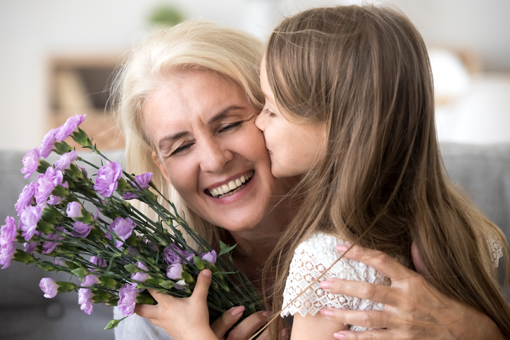 young girl kissing her grandmother on the cheek holding a bouquet of flowers
