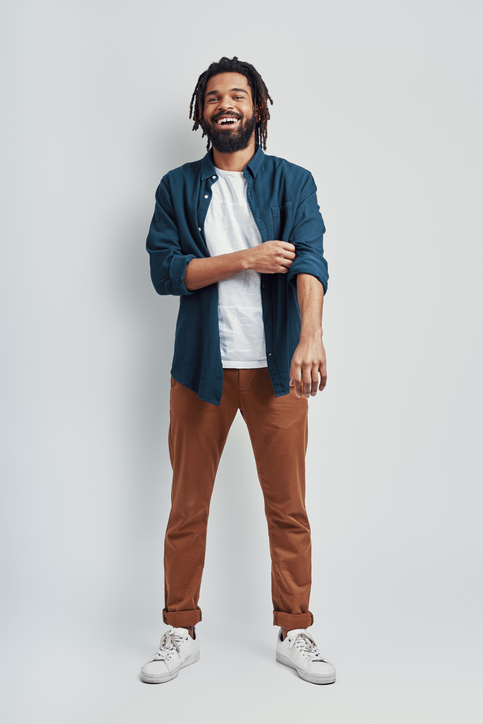 Full length of handsome young African man in casual wear adjusting sleeve and smiling while standing against grey background