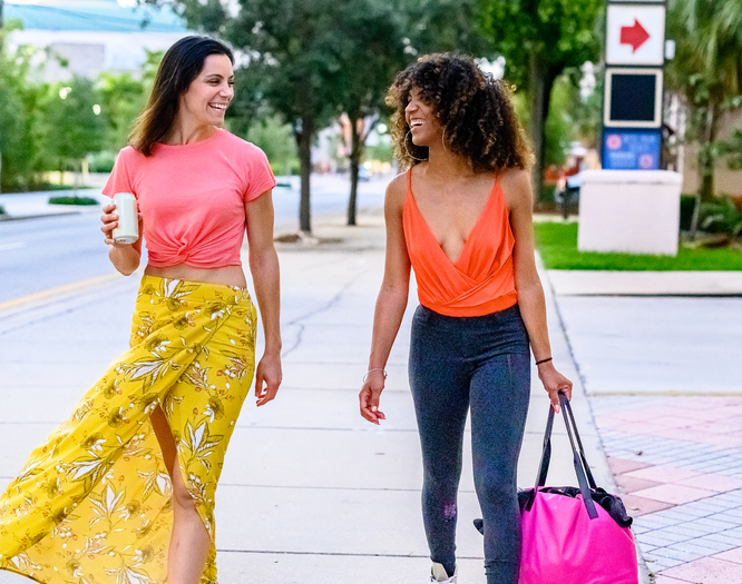 Happy young women walk down a city sidewalk in hip casual clothes