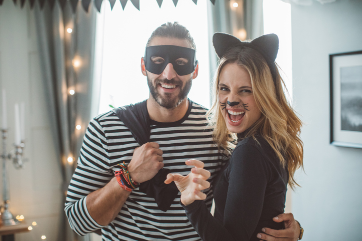 Young couple at home party celebrating Halloween in costume of thief and cat-woman