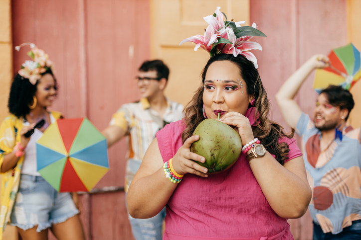 woman drinking out of a coconut dressed in pink with a floral hat topper