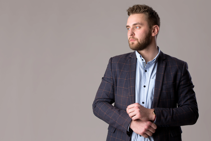 Handsome bearded man in a jacket and shirt on a gray background.