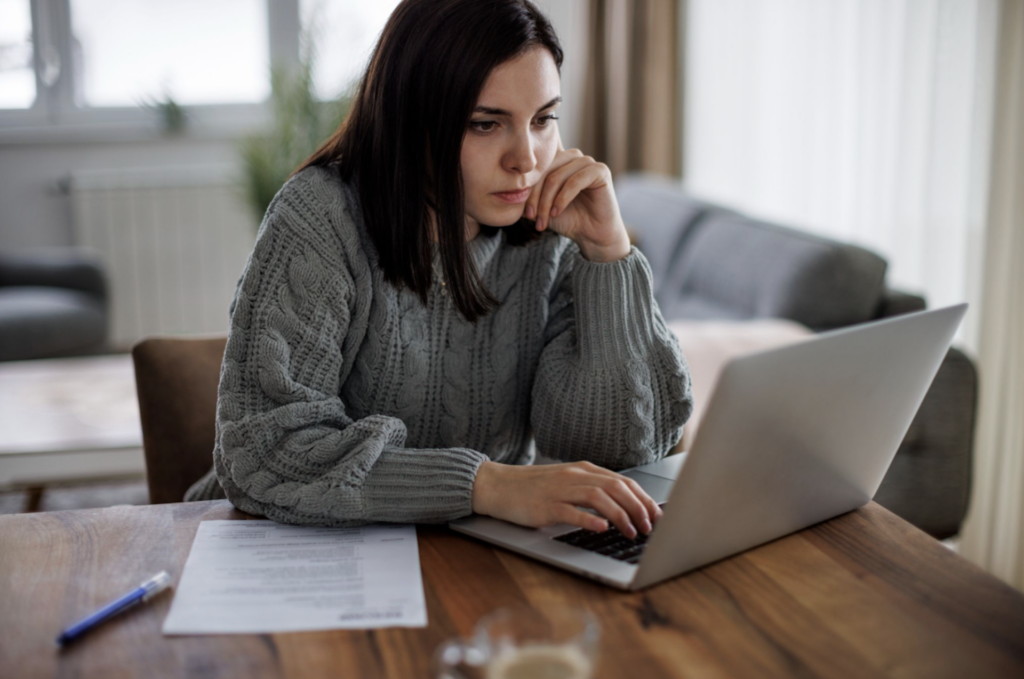 Someone sitting on a laptop with a pen and paper