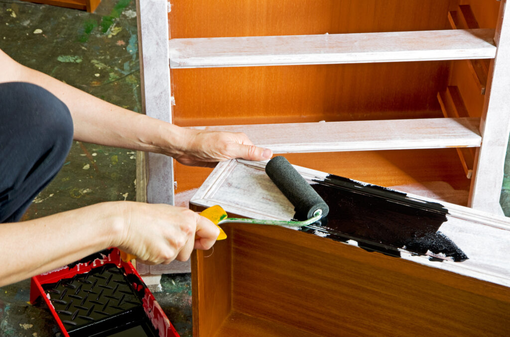 painter with paint roller painting a wooden drawer.
