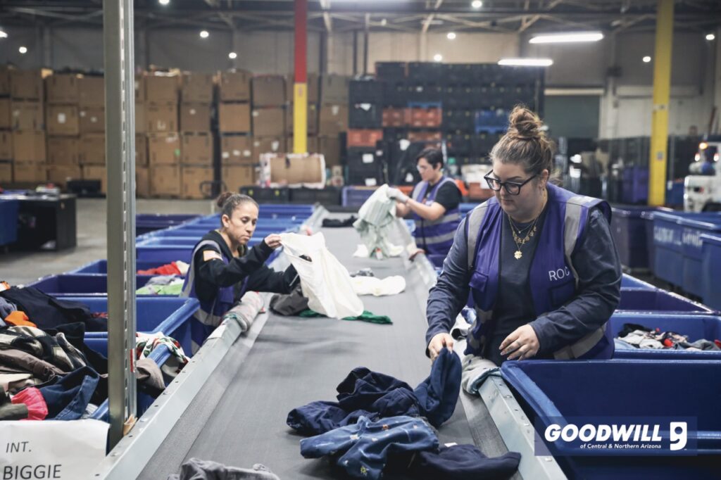 Three people in a warehouse sorting clothing from bins