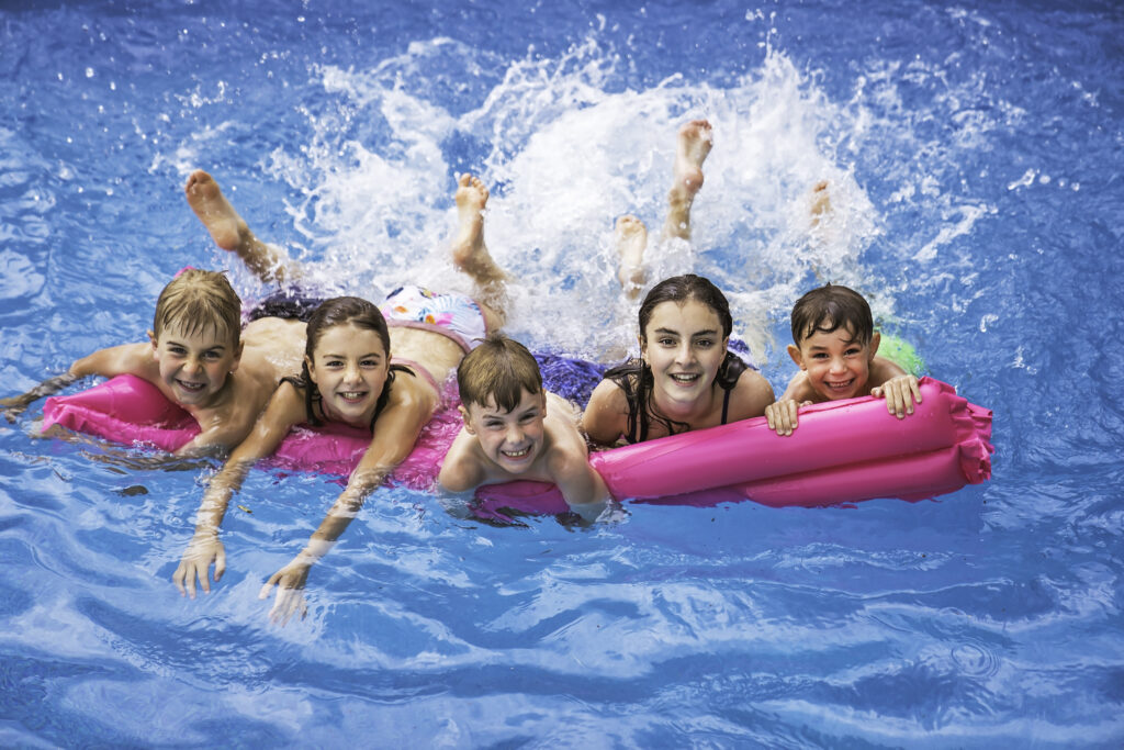 five kids laying on one float kicking in the pool