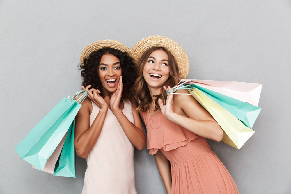 Two women smiling standing next to each other holding shopping bags