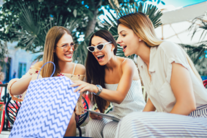 Three women smiling sitting together opening a shopping bag