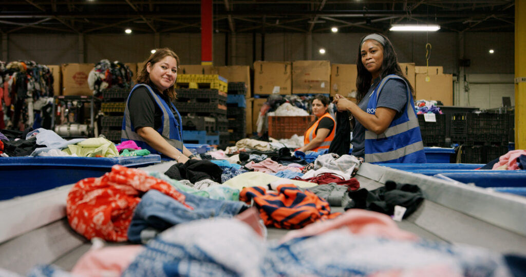 Two employees sorting clothes from bins in a warehouse