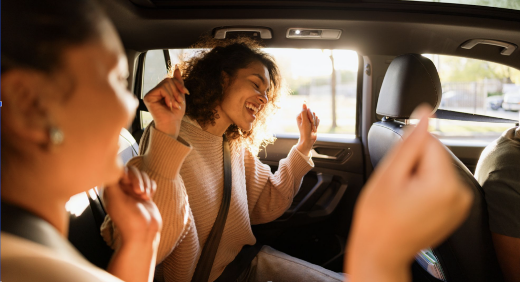 Two smiling friends singing in the back seat of a car on a road trip